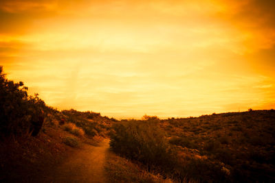 Road amidst field against sky during sunset
