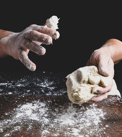 Midsection of man kneading dough against black background