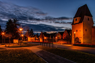 Illuminated street amidst buildings against sky at night