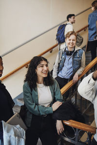 Smiling female university student with friends enjoying at staircase