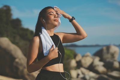 Side view of young woman looking away while standing at beach against sky