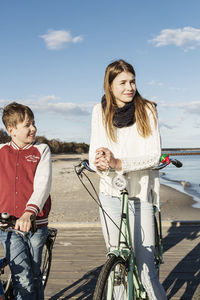 Brother and sister with bicycles looking away at beach