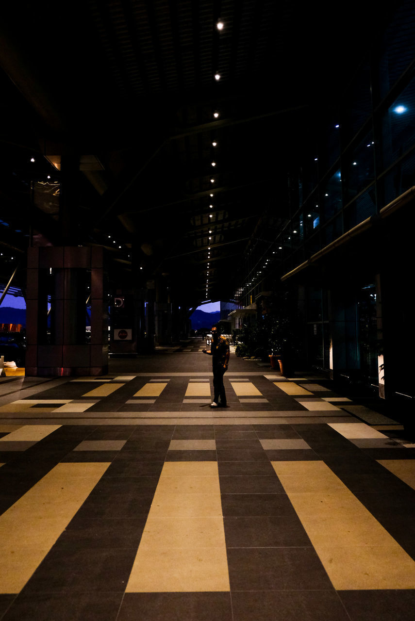 FULL LENGTH OF MAN WALKING ON ILLUMINATED ROAD AT NIGHT