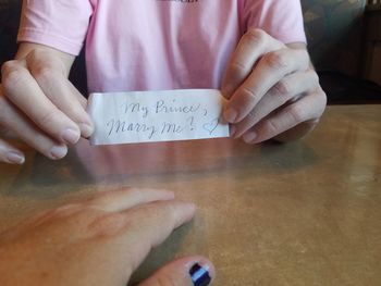 Midsection of woman holding paper with text on table