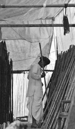 Rear view of man standing in a wood shop trying to find the right stick