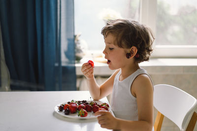 Cute beautiful little boy eating fresh cherry and strawberry.