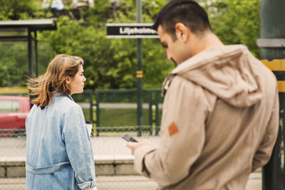 Young woman waiting while man using mobile phone at tram station