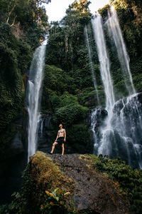 Man standing on rock against waterfall in forest
