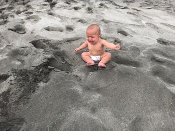 Shirtless baby boy crying while sitting on sand