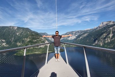 Man with arms outstretched while standing at observations point against mountains