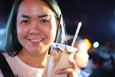 Portrait of smiling mid adult woman holding ice cream in city at night