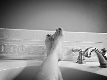 Low section of woman relaxing in bathtub at bathroom