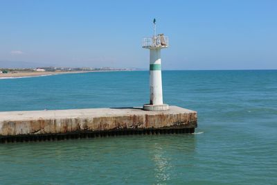 Lighthouse by sea against blue sky