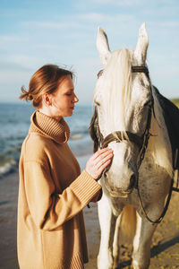 Young woman with white horse on sea beach