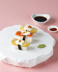 Selected focus tamago and crabstick sushi roll on white stone plate, pink background