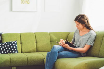 Side view of young woman using digital tablet while sitting on sofa at home