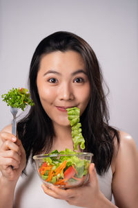 Portrait of young woman holding ice cream against gray background