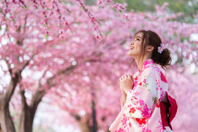 Woman standing by pink cherry blossom tree