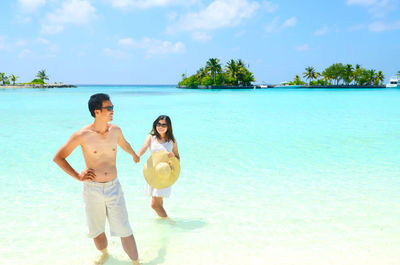 Couple wading in sea against sky