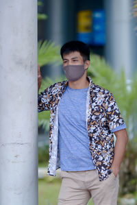 Young man in mask standing by column