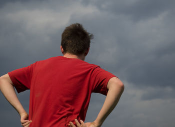 Rear view of boy in red t-shirt standing against sky