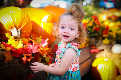 Portrait of girl on bench amidst pumpkins at park during autumn