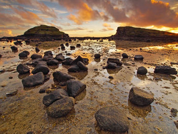 Rocks on beach against sky during sunset