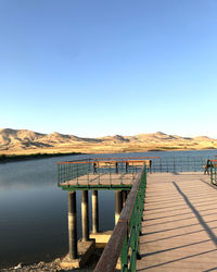 Pier over lake against clear blue sky