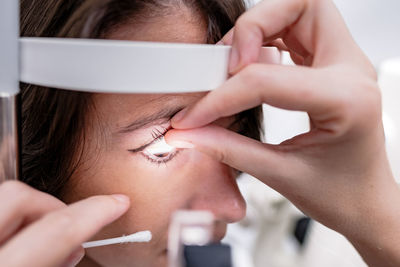 Crop ophthalmologist examining eyes of female patient with optical tonometer during appointment in modern clinic