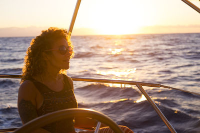 Reflection of woman on boat in sea against sky during sunset