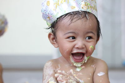 Close-up of cheerful shirtless messy baby girl wearing hat