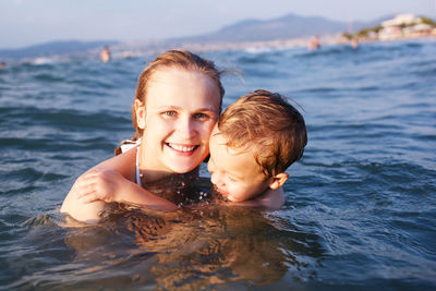 Portrait of happy mother swimming with son in sea