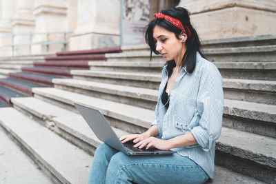 Young woman using laptop while sitting on staircase