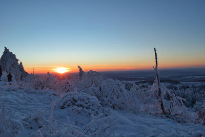 Snow covered landscape against sky during sunset