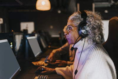 Side view of senior woman playing video game on computer in gaming center