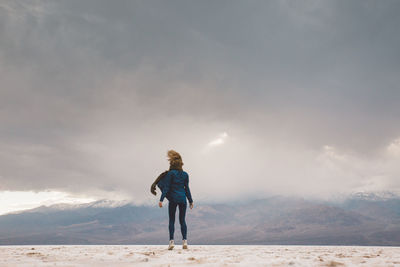 Rear view of woman standing on field against cloudy sky at death valley national park