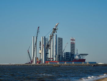 Cranes at commercial dock against clear blue sky
