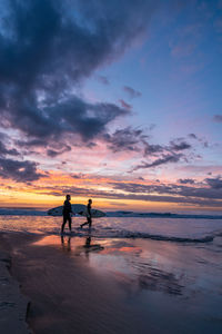 Silhouette people on beach against sky during sunset