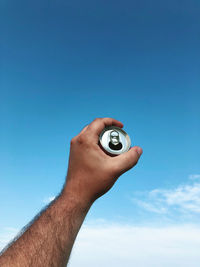 Cropped hand of person holding key against blue sky