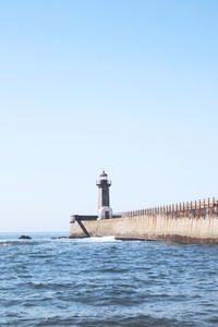 Lighthouse by sea against clear sky