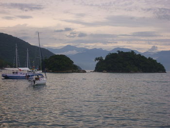 Boats in sea against cloudy sky