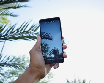 Midsection of person holding mobile phone against sky