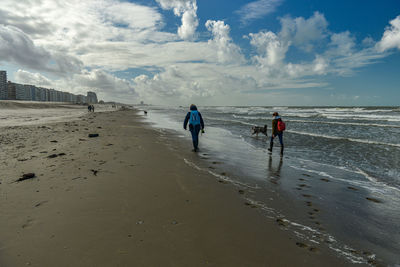 Rear view of people walking on beach against sky