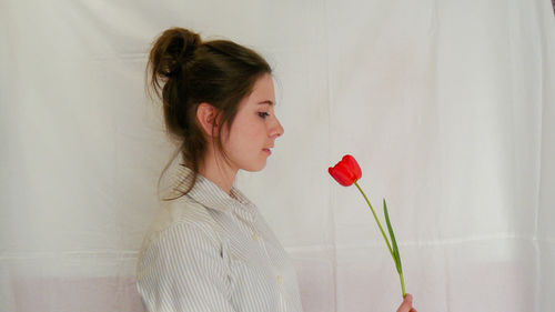 Woman holding red tulip against white wall