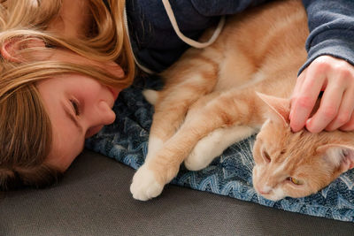 A young adolescent girl lying on a couch finds comfort by snuggling and petting her tabby cat