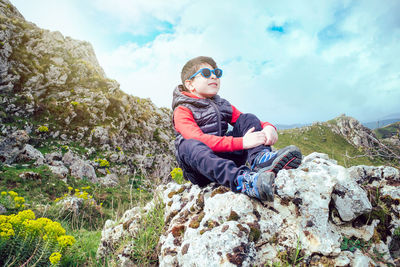 Smiling child sitting on a large rock during a mountain trek looks at the sky
