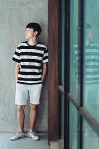 Full length of young man looking away while standing against wall