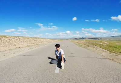 Full length of man sitting on road against blue sky