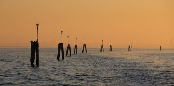 Silhouette wooden posts in sea against clear sky