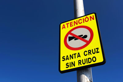 Low angle view of sign board on pole against clear blue sky